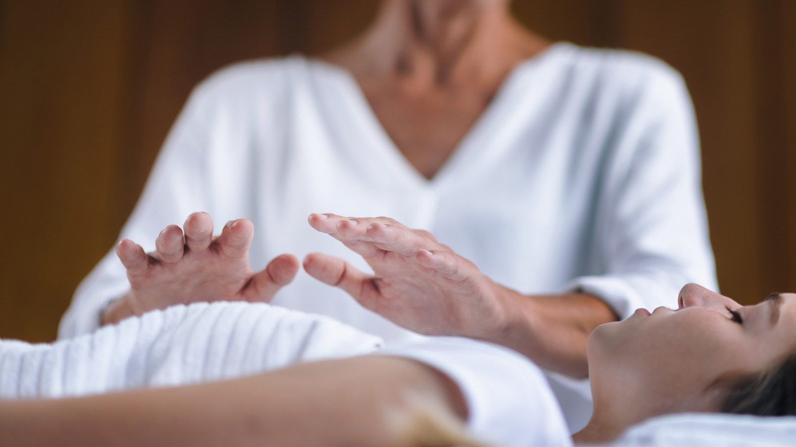 A Reiki practitioner in white, hands held just above a client resting on a treatment table.
